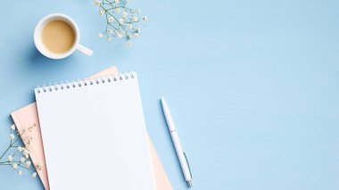 Düz uzanış, üst düzey kadın çalışma alanı boş not defteri, bir fincan kahve, mavi arka planda kalem ve çiçekler. Asgari tarz ofis masası, iş ve eğitim konsepti