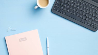 Laptop klavyeli modern ofis masası, bir fincan kahve, kağıt defter, kalem, mavi arka planda bardaklar. Yazar ya da blog yazarı çalışma alanı, düz alan, üst görünüm. İş ve teknoloji kavramı