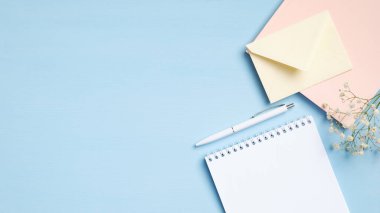 Düz uzanmış, üst kattaki ofis masasında boş not defteri, pembe defter, kalem, çiçek, mavi zemin üzerinde fotokopi alanı olan zarf. Asgari biçimdeki kadınsı çalışma alanı