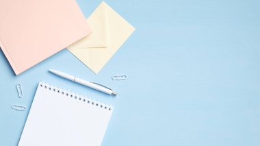 Boş not defteri, pembe kağıt defter, zarf ve mavi arka planda diğer malzemelerle modern ofis masası. Asgari stil öğrenci çalışma alanı. Eğitim ya da iş konsepti. Düz yatış, üst görünüm