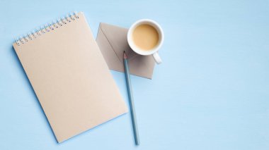 Boş not defterli modern ofis masası, bir fincan kahve, kalem, mavi arka planda zarf. Düz yerde, üst tarafta. İş konsepti