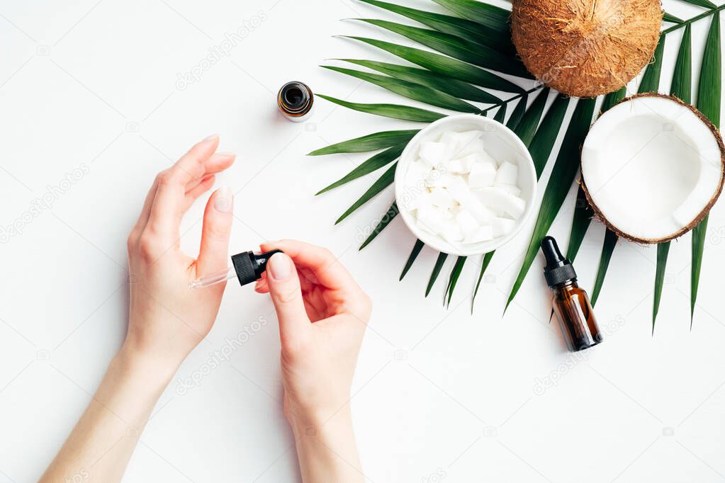 Female hands applying coconut oil for hand skin moisturizing. Flat lay composition with woman's hands, tropical palm leaf, coconuts, essential oils. Hand skincare, beauty treatment concept