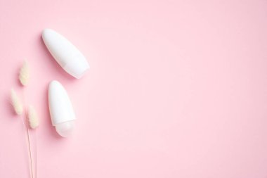 Terleme önleyici deodorant şişeleri ve pembe arka planda kuru çiçekler. Ter korumalı ürün konsepti. Düz yatış, üst görünüm