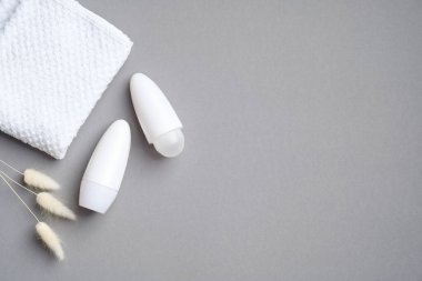 Kuru çiçekli deodorant ambalajı ve gri arka planda havlu. Boş terleme önleyici şişeler, terleme önleyici konsept. Düz yatış, üst görünüm