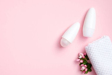 Çiçekli terleme önleyici şişeler ve pembe arka planda havlu. Düz yerde, üst tarafta. Koltuk altı cilt bakımı, ter koruması konsepti