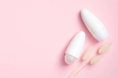 Minimum deodorant ambalajı ve pembe arka planda kuru çiçekler. Düz yerde, üst tarafta. Boş terleme önleyici şişeler, terleme önleyici ürün konsepti