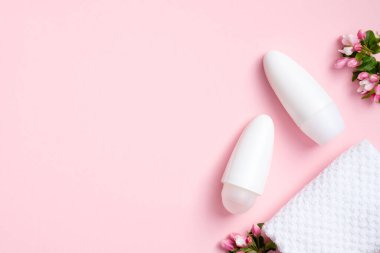 Çiçekli deodorant şişeleri ve pembe arka planda havlu. Düz yerde, üst tarafta. Koltuk altı cilt bakımı ve ter koruması için doğal organik kozmetik ambalajlar.