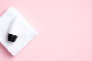 Deodorant şişesi, pembe arka planda havluyla birlikte. Düz yerde, üst tarafta. Boş terleme önleyici ambalaj, terleme önleyici ürün konsepti