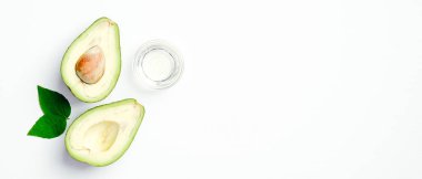 Yağlı kavanoz ve beyaz arka planda avokado. SPA doğal organik kozmetik ürünleri, cilt bakımı ve vücut tedavisi konsepti. Düz yatış, üst görünüm