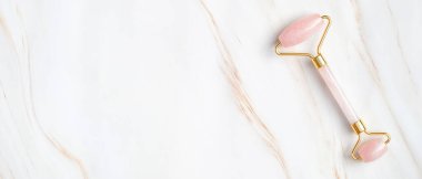 Gül kuvars yüz silindiri mermer arka planda, üst manzara. Yüz masajı aletli pankart modeli. Cilt bakımı, vücut tedavisi kavramı