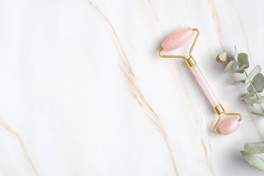 Gül kuvars yüz silindiri ve mermer arka planda okaliptüs yaprağı, üst manzara. Yüz masajı aracı, güzellik tedavisi ve yüz bakımı konsepti