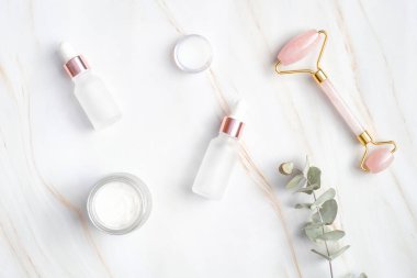 Yüz bakımı için doğal kozmetik seti. Düz uzanma, yüz masajı silindiri, damlatıcı şişelerde serum, mermer masada nemlendirici krem. SPA rahatla, yüz bakımı ve vücut bakımı