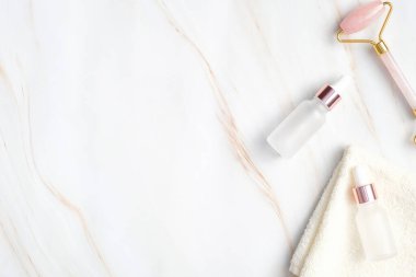 Doğal SPA kozmetik ürünleri ve yüz bakımı için ekipman içeren düz bir kompozisyon. Üst görünüm şeffaf damlalar organik yağlar, havlu, mermer zemin üzerinde yüz masajı silindiri