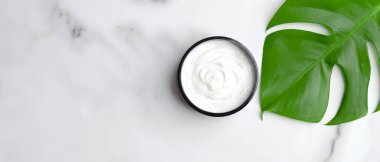 Doğal kozmetik krem nemlendirici ve mermer masa üzerinde canavar palmiye yaprağı. SPA organik güzellik ürünü. Cilt bakımı, el veya vücut bakımı konsepti. Düz yatış, üst görünüm.