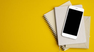 Sarı arka planda boş ekran modeli olan bir yığın defter ve akıllı telefon. Modern ofis masa üstü manzaralı. Hipster startup uygulaması konsepti.