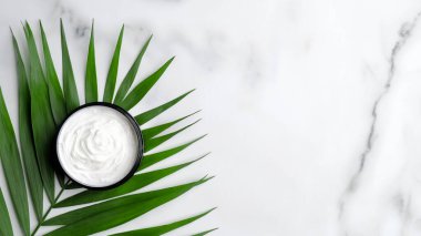 Doğal organik krem nemlendirici kavanozu mermer masada palmiye yaprağı üzerinde. Cilt bakımı. Düz yatış, üst görünüm.