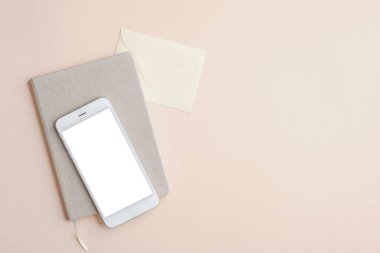 Düz uzanış, üst görünüm ofis masası cep telefonu modeli, beyaz ekran, kağıt defter ve bej arka planda zarf. İş ve teknoloji kavramı.