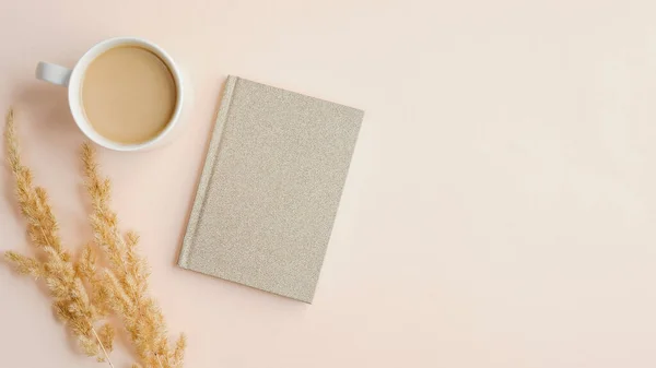 Flat lay, top view home office desk table with cup of coffee, paper notebook and dry flowers on beige background. Elegant feminine workspace, minimalistic style