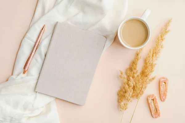 Boho tarzı, not defteri, kahve fincanı, beyaz battaniye, kuru çiçekler ve kadınsı aksesuarları olan minimal çalışma masası. Düz yatış, üst görünüm.