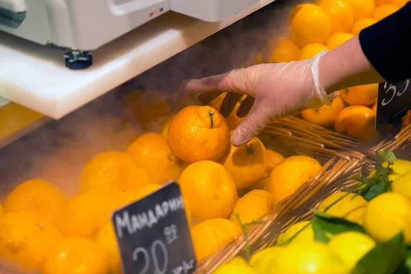 female hand picking up tangerine in supermarket store