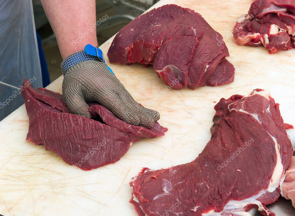Closeup of butcher man cutting veal on slices on table