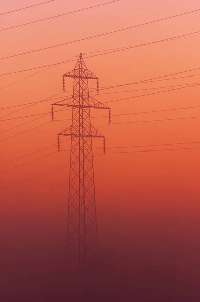 Torre de transmissão emergindo do nevoeiro em um céu laranja por do sol — Fotografia de Stock