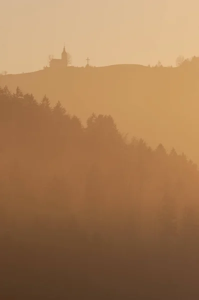 Bella vista sulle piste forestali e chiesa in cima alla collina nella foschia serale — Foto Stock