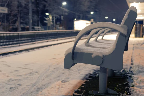 Vacant bench covered with snow at an empty train station at night — Stock Photo, Image