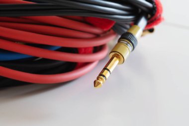 Beyaz zemin üzerinde altın trs telefon kriko ses bağlantısıyla sarılı ses kabloları. Müzik, ses, hi-fi, bağlantı ve ses üretimi.