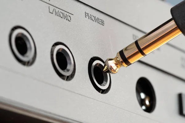 Golden TRS phone jack audio connector being plugged into phones socket on audio device. Music, audio, hi-fi, connectivity and sound reproduction.