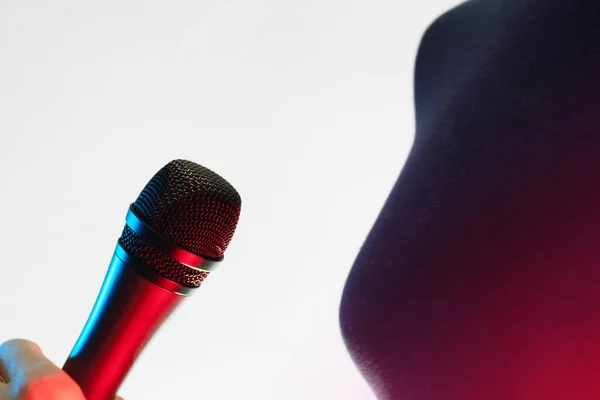 Closeup of woman holding a blue and red illuminated vocal microphone on white background. Music, singing, disco, karaoke and sound reproduction.