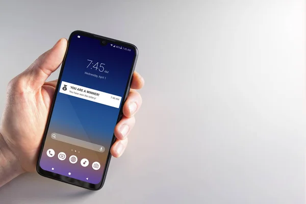 1 Nisan 'da piyango talihlisinin bildirdiği akıllı telefonu tutan bir erkek. Dolandırıcılık, Nisan şakaları, siber suçlar, gizlilik ve teknoloji kavramları.