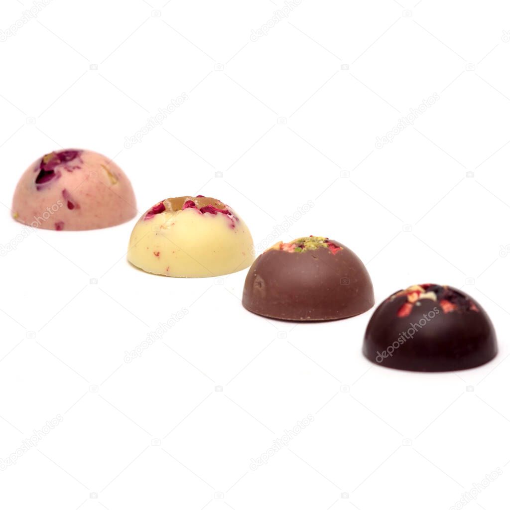 Handmade white, milk and dark chocolate candies with a variety of dried fruit and nut toppings on a white background