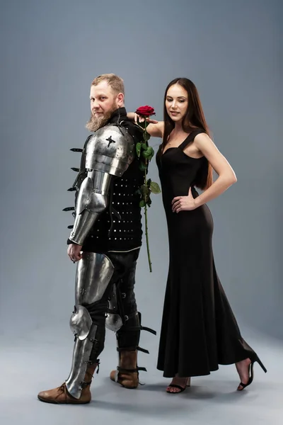 黒のドレスの美しい女の子と赤いバラ彼女の手に鎧の騎士の横にある — ストック写真