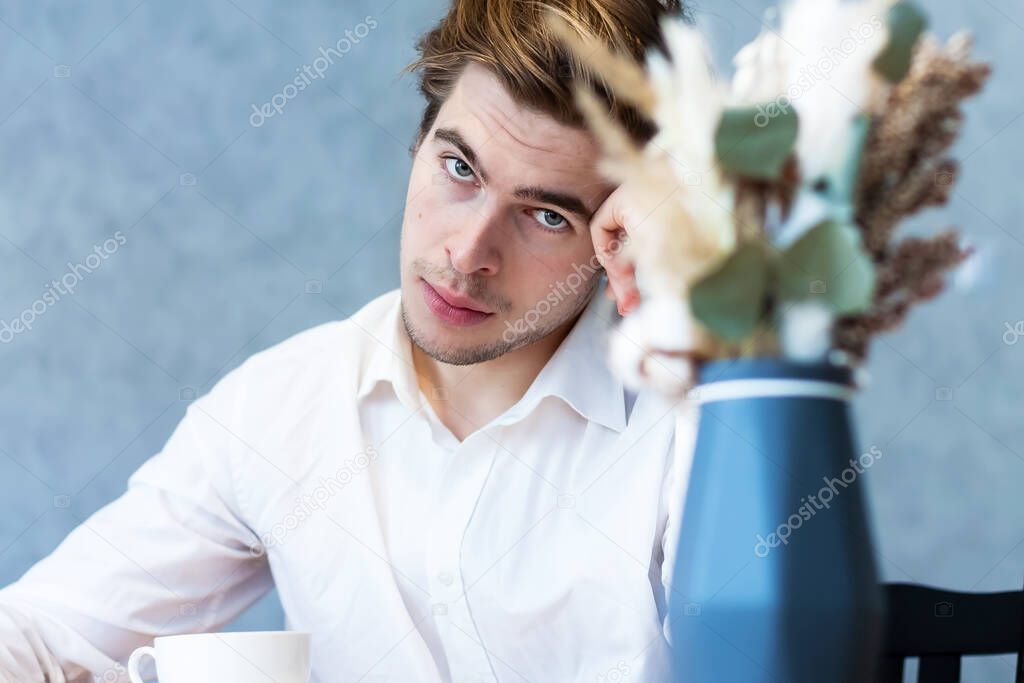 Handsome pensive male in white shirt looking away sitting at table in cafeteria thinking about plans, caucasian guy waiting for meeting in coffee shop dreaming about idea on leisure