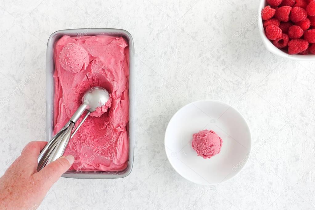 Hand Scooping Raspberry Ice Cream from Tub 