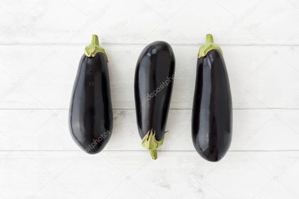 Three Whole Aubergines on White Wood Background     