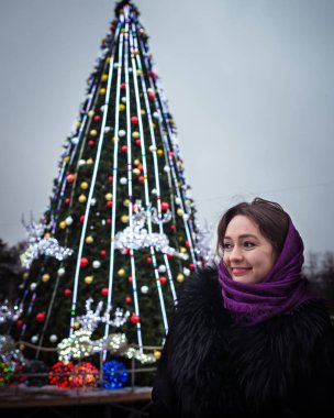 Genç güzel kadın bir arka plan bir Noel köknar ağacı, uzakta görünüyor ve gülümsüyor üzerinde duruyor. Yeni yıl arifesinde. Bir kişi