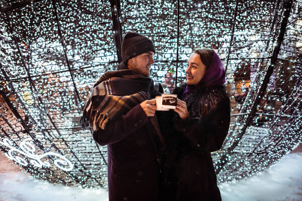 Couple celebrating Christmas with cups of hot tea near holidays decorations. Cheers!