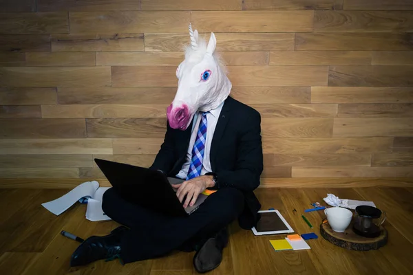 Unicorn in a suit and tie smiles and using laptop