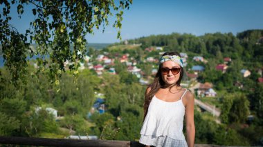 Sunglass ve beyaz elbise genç kadın bir tepede duruyor