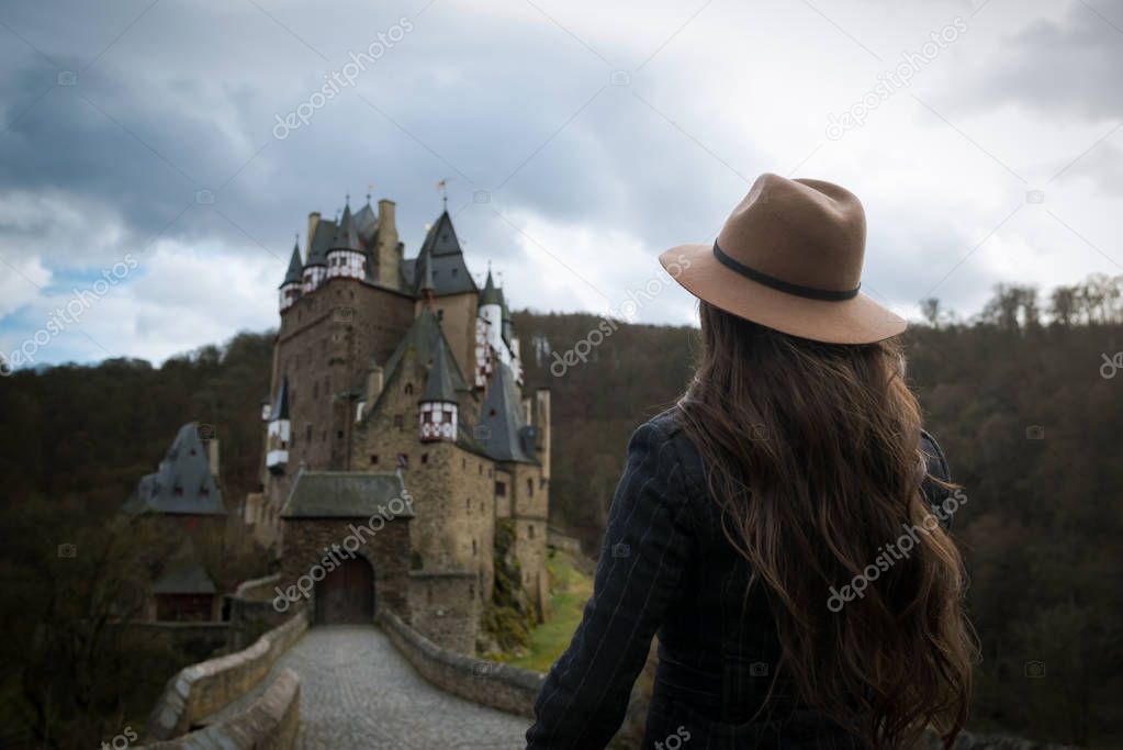 Young unrecognizable woman walks along the road leading to a incredible castle