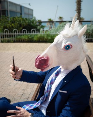 Tek boynuzlu at telefonla bir fotoğraf yapar. Komik maskeli genç sıradışı adam