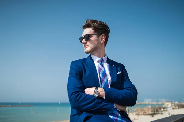 Young serious man in elegant suit and sunglass on the background of the sea