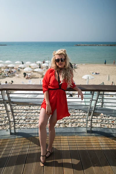 Mujer atractiva joven en vestido rojo brillante se encuentra en el paseo marítimo de la ciudad — Foto de Stock