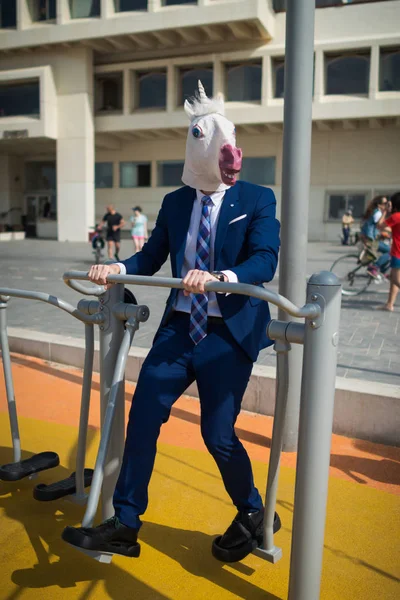 Freaky man in elegant suit and funny mask does sport exercises