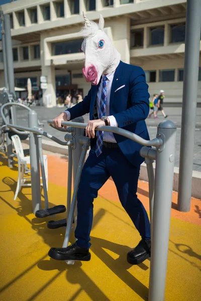 Funny man in elegant suit and comical mask does sport exercises