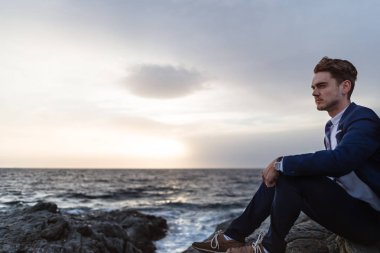 Deniz kenarı Okyanusu yakınlarındaki şık elbiseli ciddi genç adam oturur