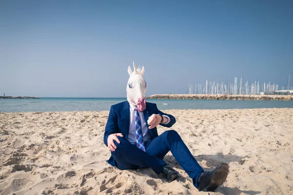 Hombre serio en máscara cómica se sienta en la arena y disfruta de un día soleado — Foto de Stock