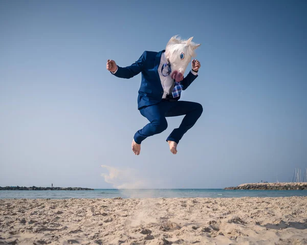 Stylish man in funny mask and suit jumps on beach